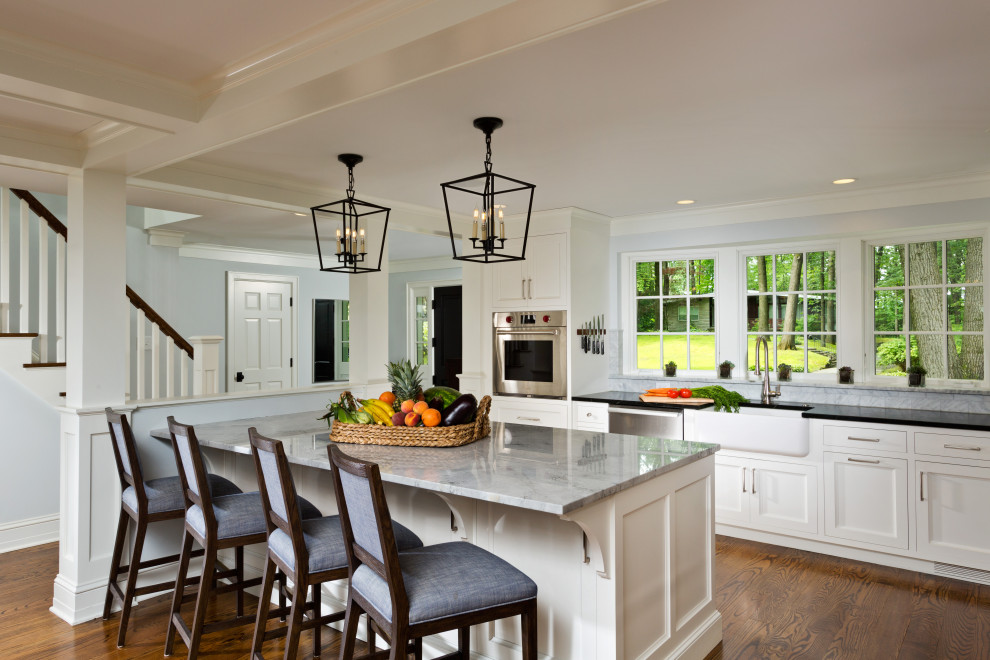 Photo of an expansive traditional l-shaped eat-in kitchen in Boston with a farmhouse sink, beaded inset cabinets, white cabinets, marble benchtops, grey splashback, marble splashback, stainless steel appliances, medium hardwood floors, with island, brown floor, grey benchtop and coffered.