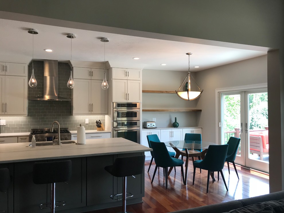 Mid-sized transitional single-wall medium tone wood floor and brown floor eat-in kitchen photo with an undermount sink, shaker cabinets, white cabinets, quartzite countertops, gray backsplash, glass tile backsplash, stainless steel appliances, an island and multicolored countertops