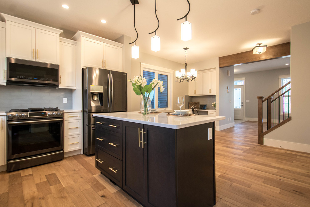 Large transitional l-shaped medium tone wood floor and brown floor enclosed kitchen photo in Calgary with an undermount sink, shaker cabinets, white cabinets, marble countertops, gray backsplash, subway tile backsplash, black appliances, an island and white countertops