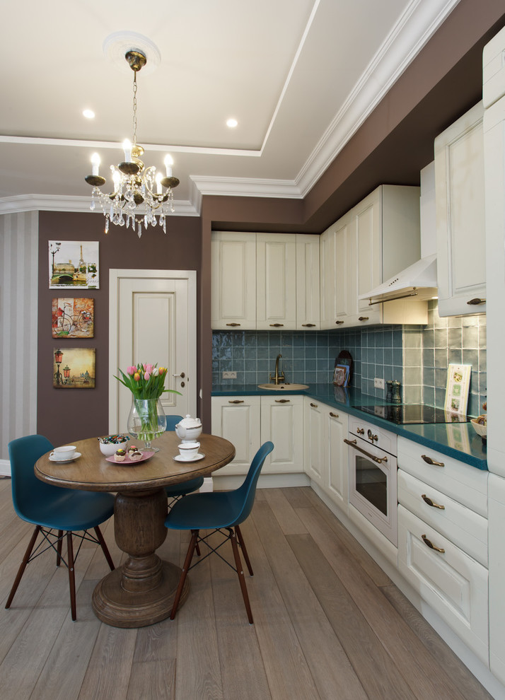 Contemporary l-shaped open plan kitchen in Moscow with a drop-in sink, white cabinets, blue splashback, ceramic splashback, white appliances and light hardwood floors.