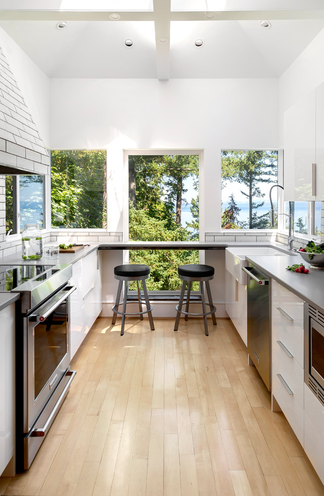 Design ideas for a small transitional u-shaped kitchen in Other with a farmhouse sink, flat-panel cabinets, white cabinets, quartz benchtops, white splashback, terra-cotta splashback, stainless steel appliances, light hardwood floors, beige floor, grey benchtop and no island.