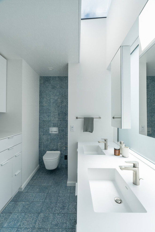This is an example of a mid-sized modern kids bathroom in San Francisco with flat-panel cabinets, white cabinets, an alcove tub, a shower/bathtub combo, a wall-mount toilet, blue tile, cement tile, white walls, cement tiles, an integrated sink, solid surface benchtops, blue floor, white benchtops, a niche, a double vanity and a built-in vanity.