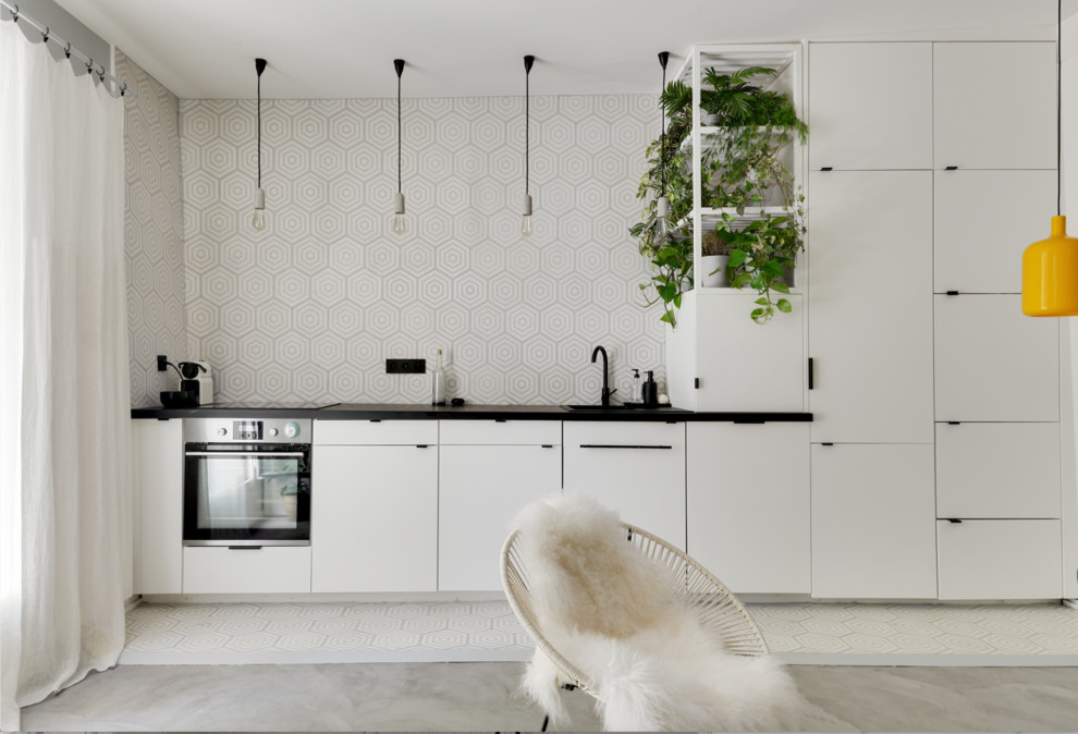 This is an example of a mid-sized scandinavian single-wall open plan kitchen in Paris with a single-bowl sink, flat-panel cabinets, white cabinets, multi-coloured splashback, stainless steel appliances, no island, black benchtop, concrete floors and grey floor.