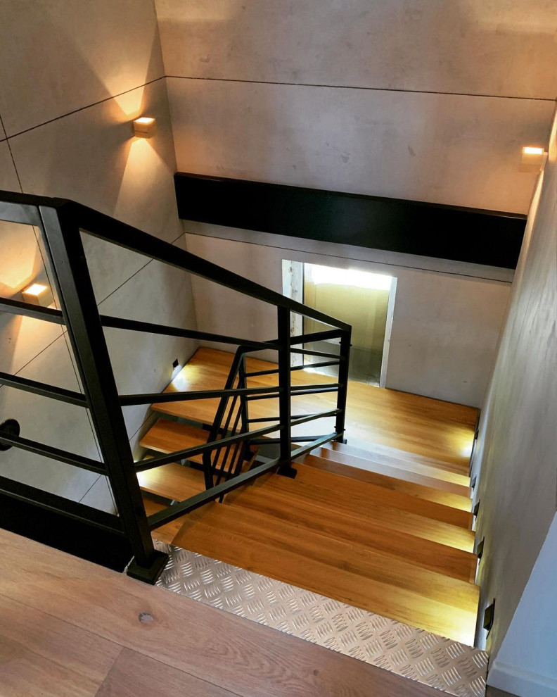 Cette image montre un escalier design en U de taille moyenne avec des marches en bois, des contremarches en bois et un garde-corps en métal.