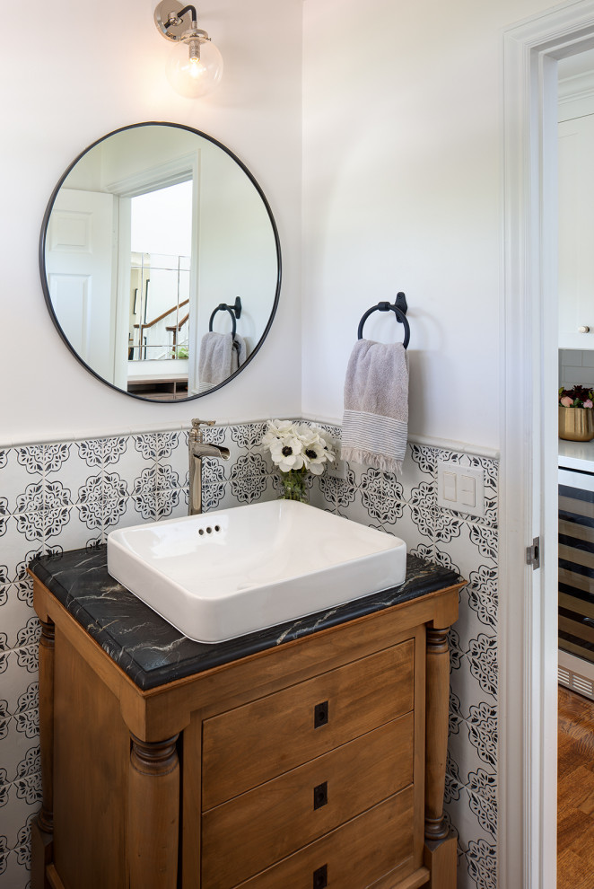 Design ideas for a small country cloakroom in San Diego with freestanding cabinets, brown cabinets, black and white tiles, ceramic tiles, white walls, a vessel sink, marble worktops, black worktops, a freestanding vanity unit, medium hardwood flooring and brown floors.