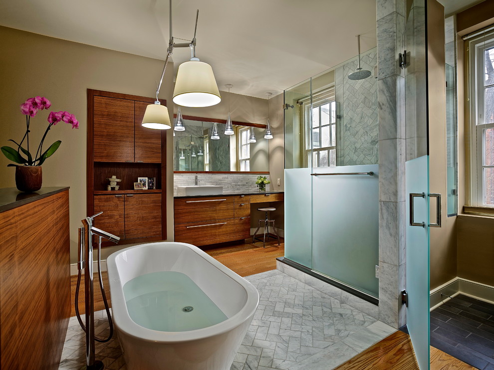 Inspiration for a mid-sized contemporary master bathroom in Philadelphia with a vessel sink, flat-panel cabinets, dark wood cabinets, a freestanding tub, a corner shower, gray tile, beige walls, medium hardwood floors, a two-piece toilet, marble, marble benchtops, brown floor and a hinged shower door.