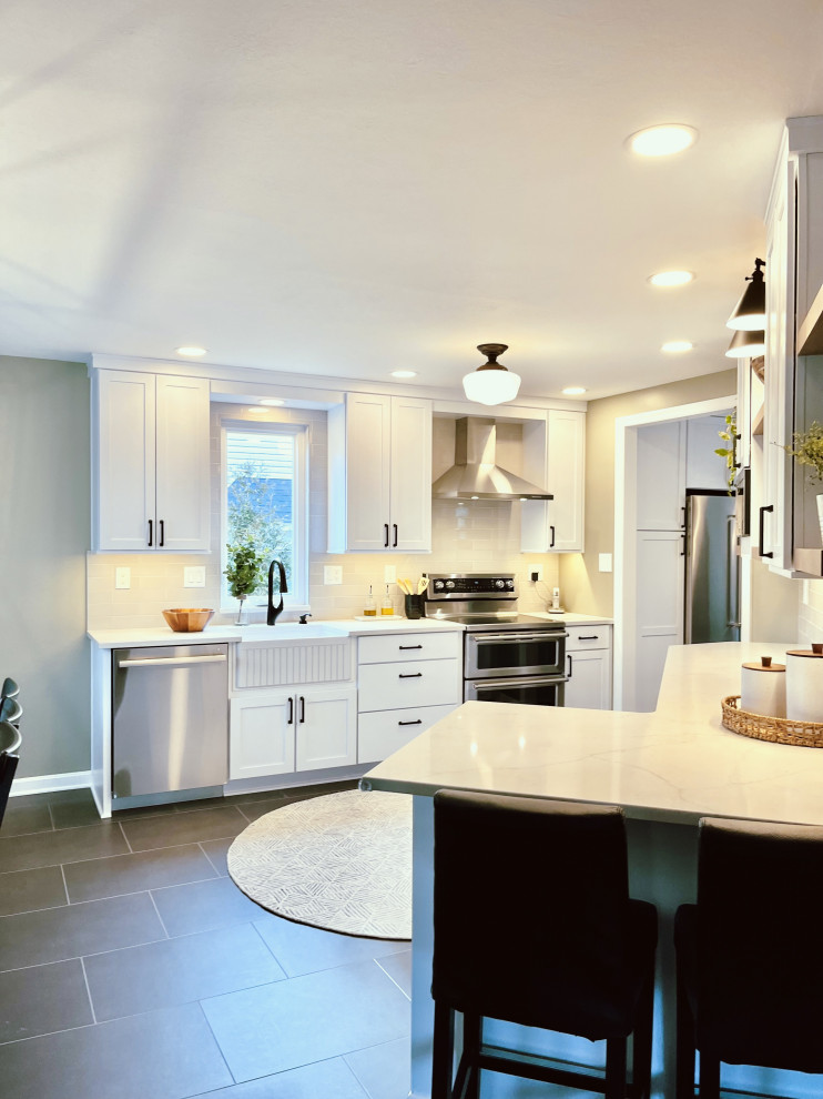 Inspiration for a mid-sized transitional l-shaped vinyl floor and black floor eat-in kitchen remodel with a farmhouse sink, shaker cabinets, white cabinets, quartz countertops, gray backsplash, ceramic backsplash, stainless steel appliances, a peninsula and gray countertops