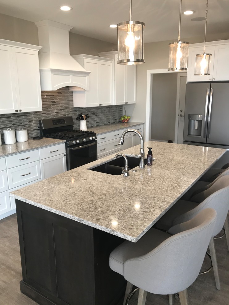 Large transitional l-shaped open concept kitchen photo in Cedar Rapids with an undermount sink, flat-panel cabinets, white cabinets, quartz countertops, gray backsplash, glass tile backsplash, stainless steel appliances, an island and gray countertops