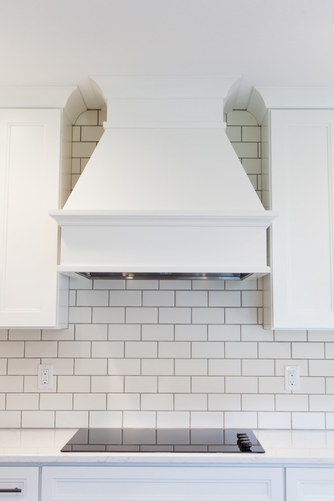 Large transitional l-shaped dark wood floor and brown floor home design photo with an undermount sink, recessed-panel cabinets, white cabinets, quartz countertops, white backsplash, subway tile backsplash, stainless steel appliances and an island