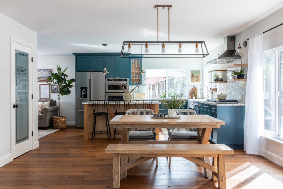 Photo of a medium sized rural l-shaped kitchen/diner in San Francisco with a belfast sink, shaker cabinets, light wood cabinets, ceramic splashback, stainless steel appliances, dark hardwood flooring, an island, brown floors and white worktops.