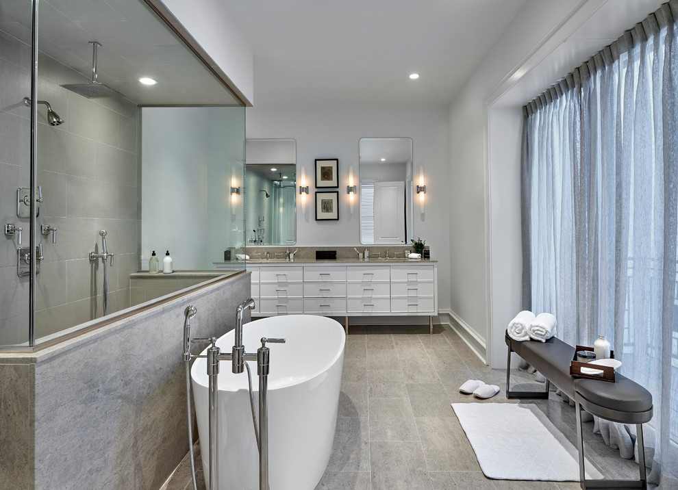 This is an example of an expansive contemporary master bathroom in Chicago with white cabinets, a freestanding tub, gray tile, grey floor, grey benchtops, grey walls, a double shower, limestone, wood-look tile, an undermount sink, limestone benchtops, an open shower, a double vanity, a freestanding vanity and flat-panel cabinets.