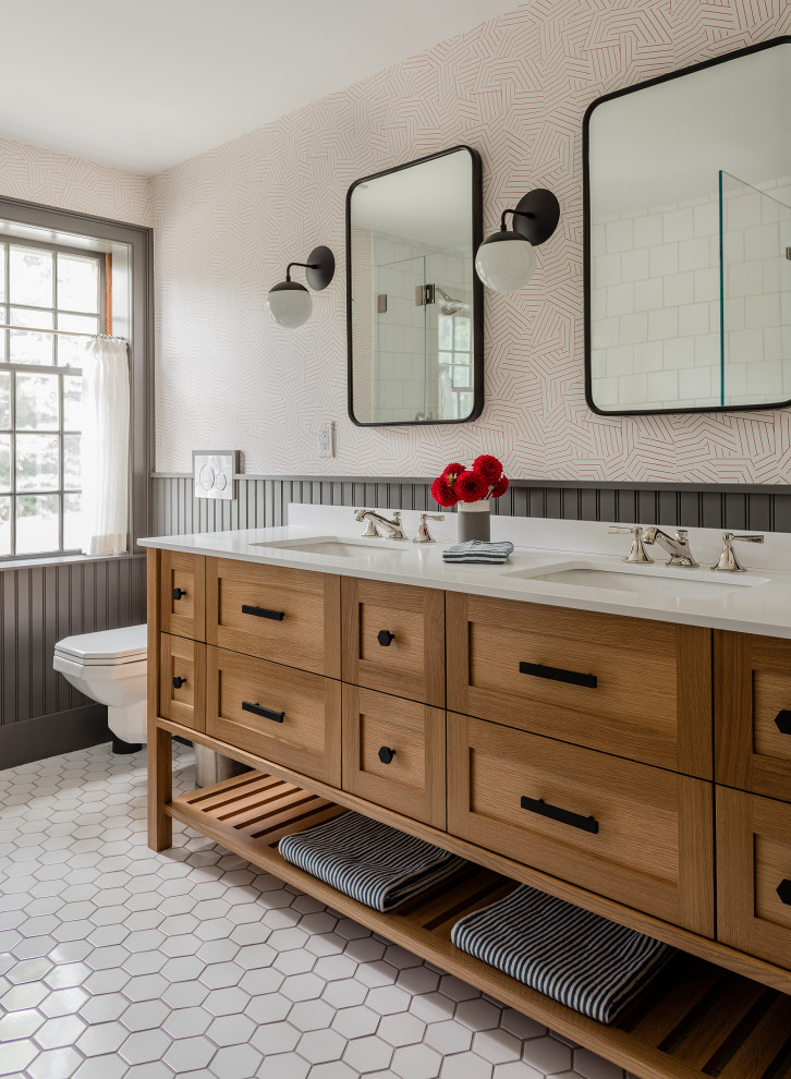 Photo of a mid-sized transitional master bathroom in Boston with white tile, ceramic tile, ceramic floors, an undermount sink, white benchtops, a double vanity, a freestanding vanity, shaker cabinets, medium wood cabinets, an alcove shower, a wall-mount toilet, multi-coloured walls, white floor, a hinged shower door, panelled walls and wallpaper.