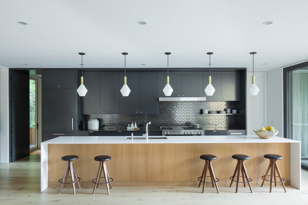Design ideas for a midcentury galley open plan kitchen in Portland with an undermount sink, flat-panel cabinets, black cabinets, metallic splashback, mosaic tile splashback, panelled appliances, light hardwood floors, with island, beige floor and white benchtop.