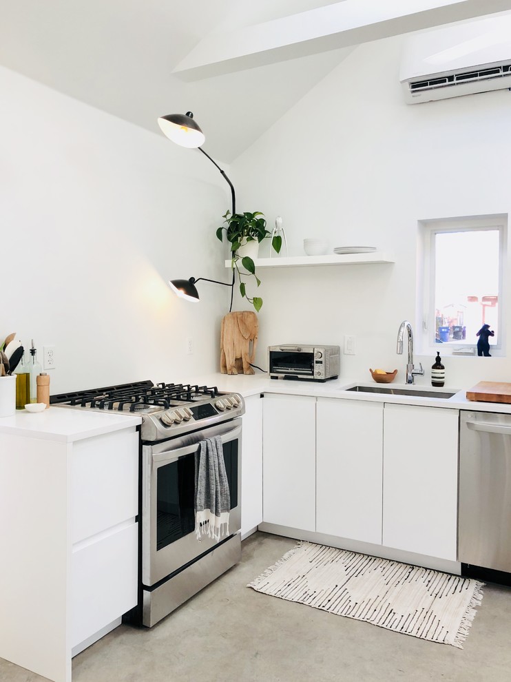 Scandinavian l-shaped kitchen in San Diego with an undermount sink, flat-panel cabinets, white cabinets, stainless steel appliances, concrete floors, grey floor and white benchtop.