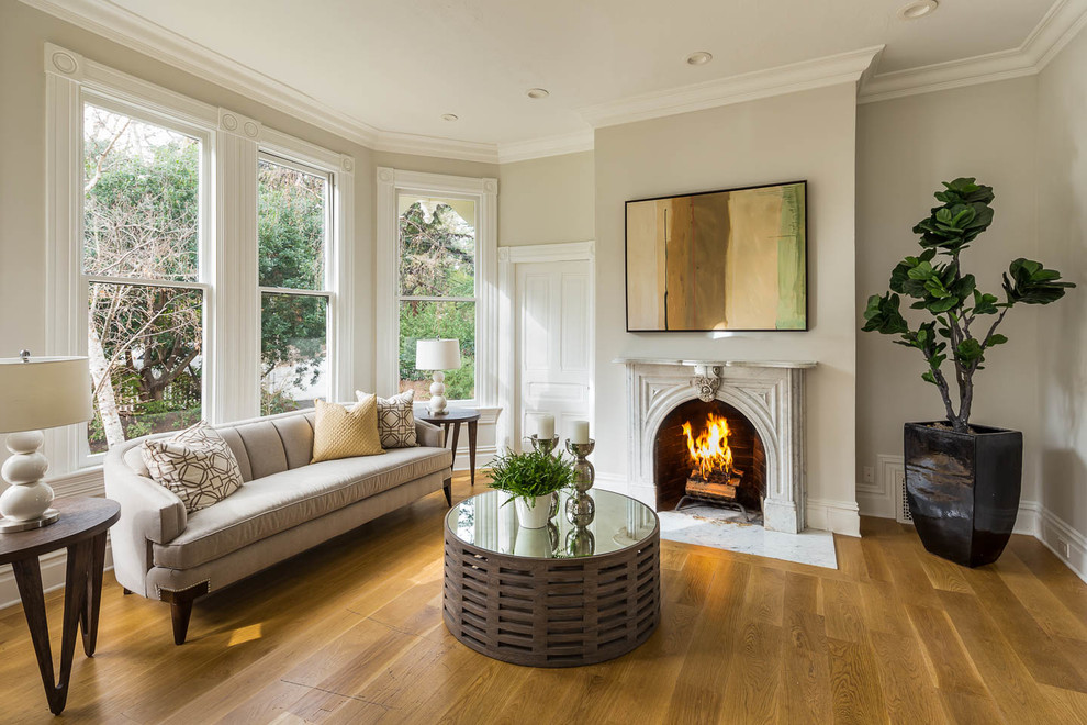 Inspiration for a mid-sized traditional enclosed living room in San Francisco with beige walls, light hardwood floors, a standard fireplace and a plaster fireplace surround.