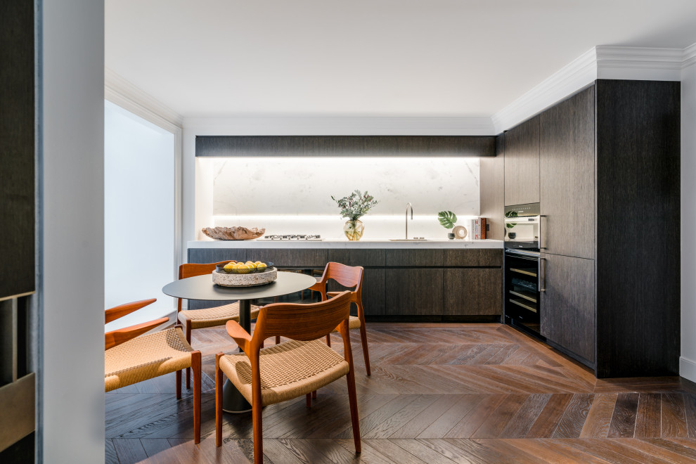 Photo of a medium sized contemporary l-shaped kitchen/diner in London with a submerged sink, flat-panel cabinets, brown cabinets, marble worktops, white splashback, marble splashback, black appliances, dark hardwood flooring, no island, brown floors and white worktops.