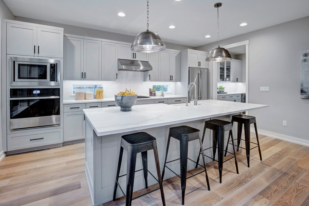 Design ideas for an arts and crafts eat-in kitchen in Seattle with a farmhouse sink, grey cabinets, quartzite benchtops, white splashback, porcelain splashback, stainless steel appliances, light hardwood floors and white benchtop.