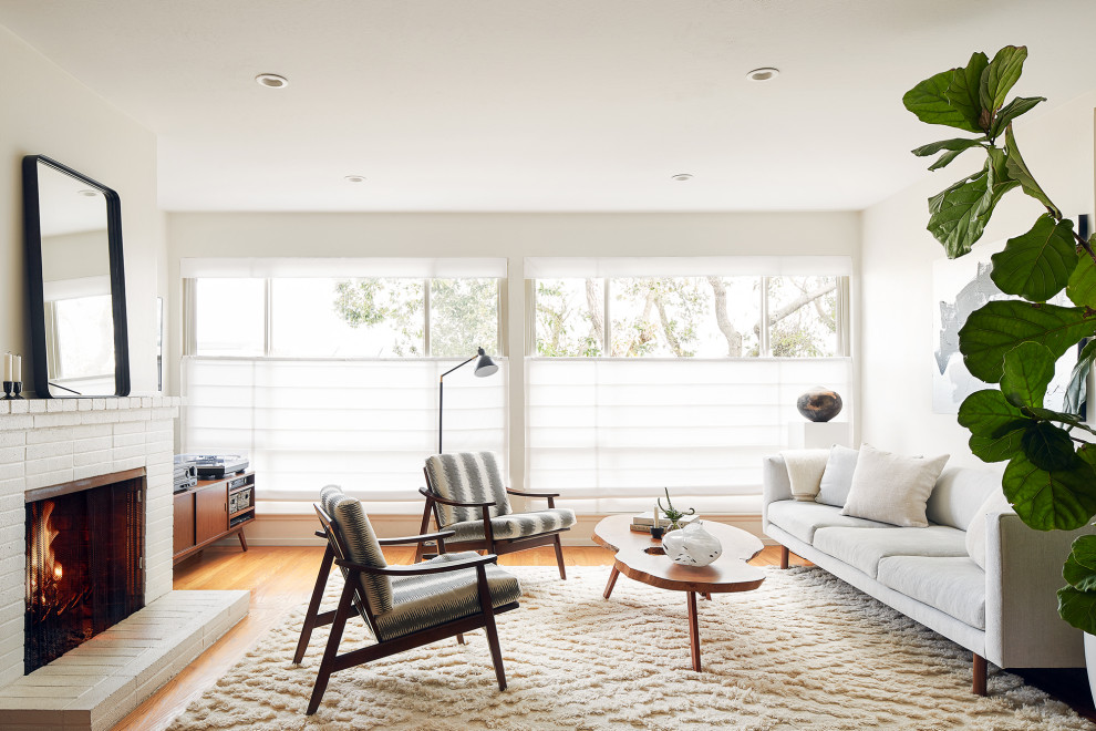 Idee per un soggiorno minimalista di medie dimensioni con pareti bianche, pavimento in legno massello medio, camino classico, cornice del camino in mattoni e pavimento marrone