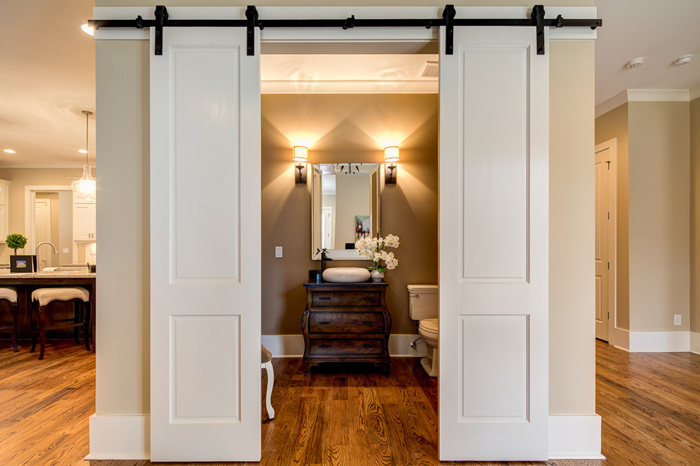 This is an example of a traditional powder room in Atlanta with furniture-like cabinets, dark wood cabinets, a two-piece toilet, brown walls, dark hardwood floors, a vessel sink, brown floor and black benchtops.