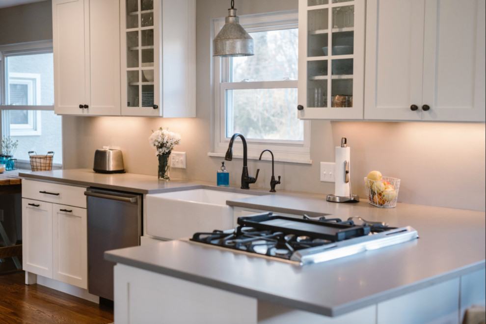 Example of a mid-sized transitional l-shaped medium tone wood floor and brown floor eat-in kitchen design in Columbus with a farmhouse sink, shaker cabinets, white cabinets, solid surface countertops, gray backsplash, matchstick tile backsplash, stainless steel appliances and no island