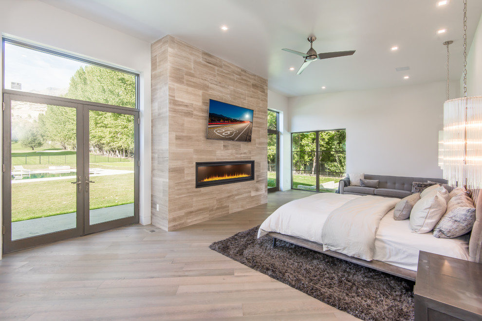 This is an example of a large modern master bedroom in Salt Lake City with white walls, light hardwood floors, a ribbon fireplace, a tile fireplace surround and white floor.