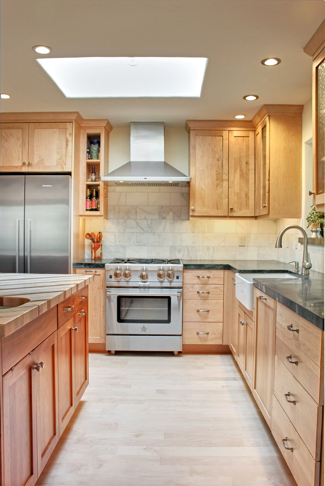 Inspiration for a mid-sized transitional l-shaped light wood floor and brown floor eat-in kitchen remodel with a farmhouse sink, shaker cabinets, light wood cabinets, soapstone countertops, white backsplash, marble backsplash, stainless steel appliances and an island
