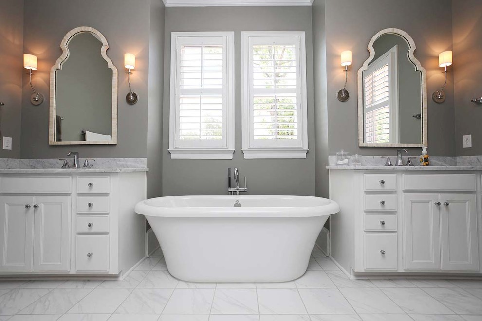 Photo of a large traditional master bathroom in Charlotte with an undermount sink, recessed-panel cabinets, white cabinets, marble benchtops, a freestanding tub, an alcove shower, white tile, stone tile, grey walls and marble floors.