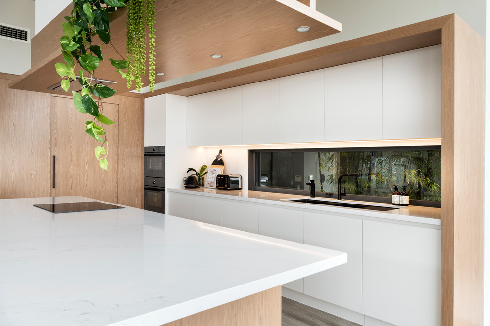 Inspiration for a large modern l-shaped eat-in kitchen in Perth with an undermount sink, recessed-panel cabinets, light wood cabinets, solid surface benchtops, white splashback, stone slab splashback, black appliances, porcelain floors, with island, grey floor and white benchtop.