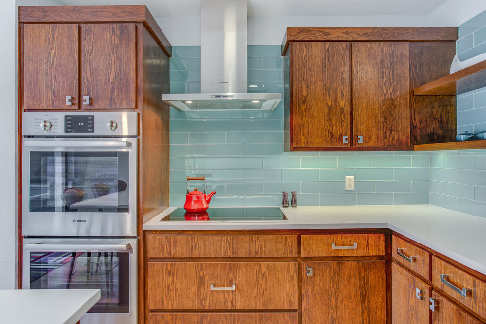 Mid-sized midcentury l-shaped eat-in kitchen in Dallas with flat-panel cabinets, medium wood cabinets, quartz benchtops, blue splashback, glass tile splashback, stainless steel appliances, a peninsula and white benchtop.