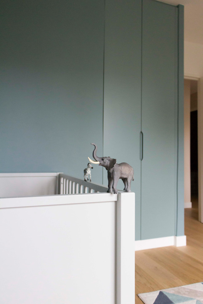 Réalisation d'une grande chambre de bébé neutre design avec un mur bleu, parquet clair et un sol marron.
