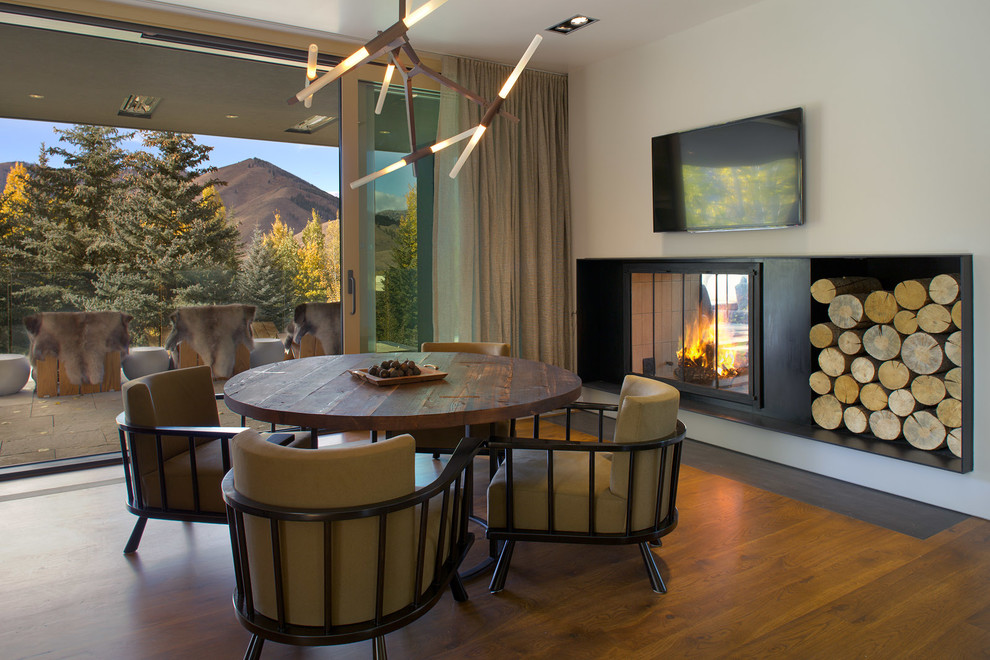 This is an example of a large contemporary dining room in Boise with white walls, medium hardwood floors, a hanging fireplace, a metal fireplace surround and brown floor.