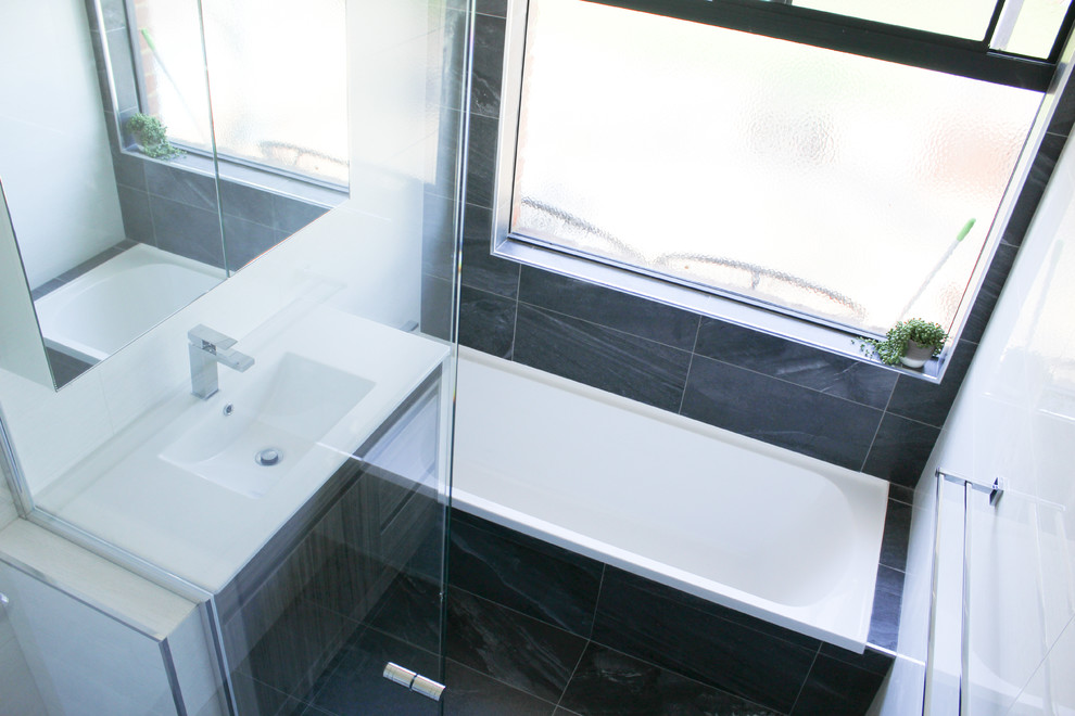 Small modern kids bathroom in Perth with furniture-like cabinets, brown cabinets, a drop-in tub, a corner shower, white tile, ceramic tile, white walls, porcelain floors, an integrated sink, solid surface benchtops, black floor, a hinged shower door and yellow benchtops.