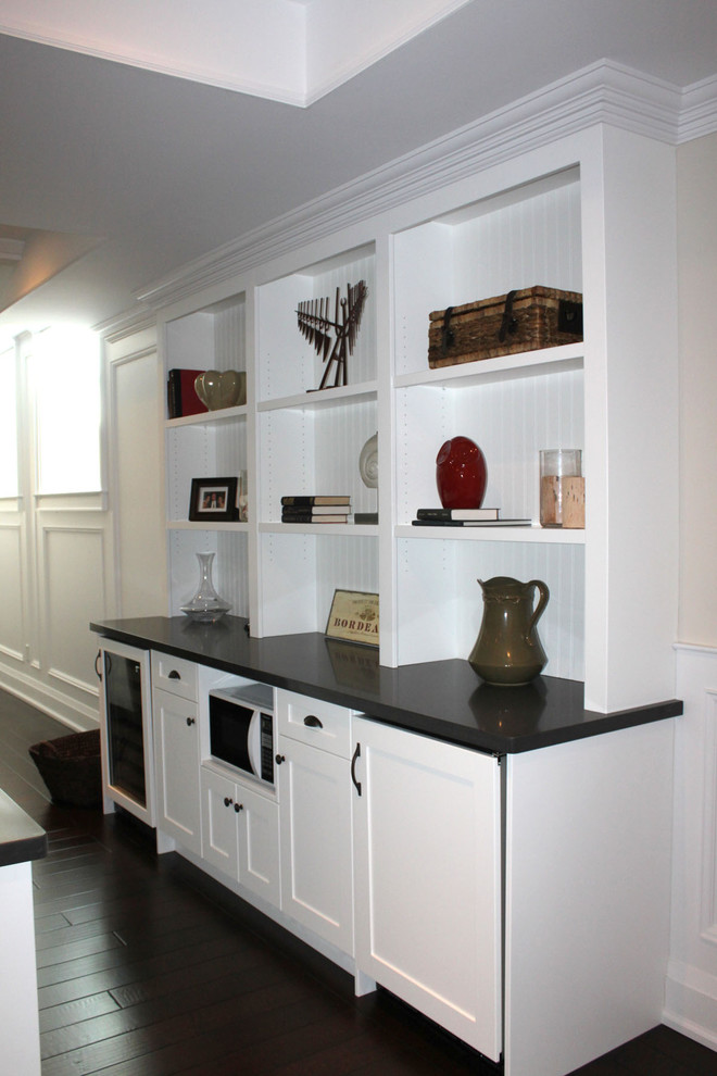 This is an example of a mid-sized traditional galley seated home bar in Toronto with no sink, recessed-panel cabinets, white cabinets, marble benchtops, dark hardwood floors, brown floor, white splashback and timber splashback.