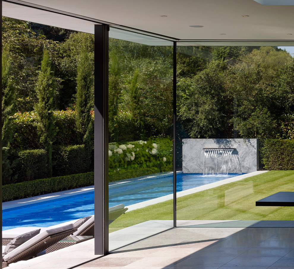 Design ideas for a contemporary backyard rectangular lap pool in London with a water feature.