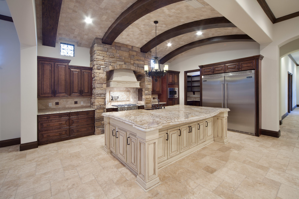 Photo of a large mediterranean open plan kitchen in Orlando with a farmhouse sink, raised-panel cabinets, dark wood cabinets, granite benchtops, beige splashback, stone tile splashback, stainless steel appliances, travertine floors and with island.