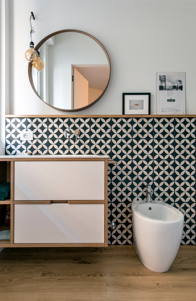 Photo of a mid-sized scandinavian master bathroom in Milan with flat-panel cabinets, light wood cabinets, an alcove shower, a two-piece toilet, black and white tile, terra-cotta tile, white walls, concrete floors, an integrated sink, solid surface benchtops, grey floor, a hinged shower door and white benchtops.
