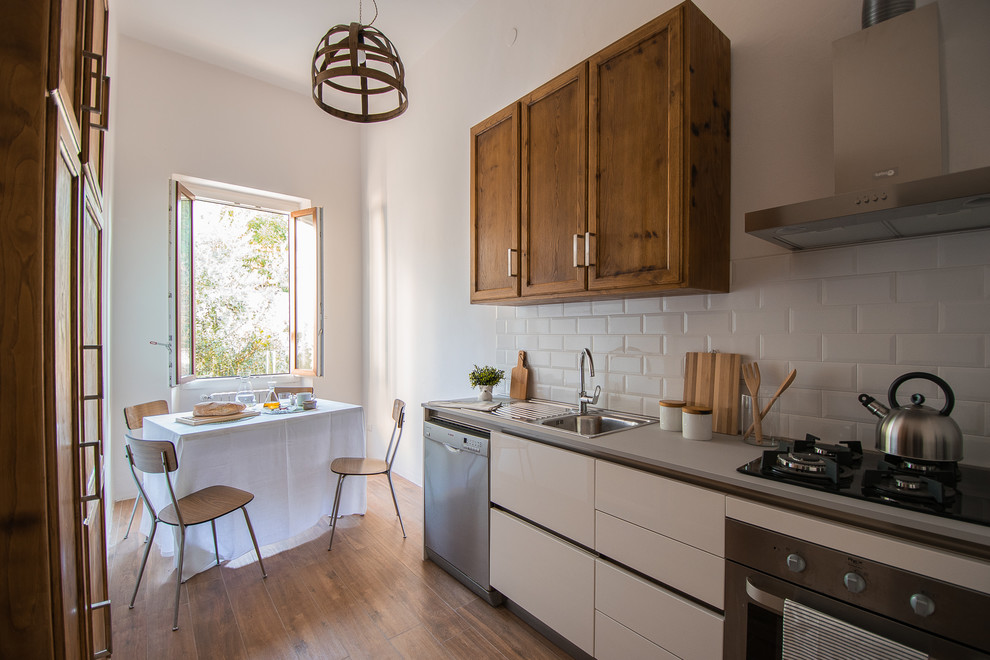 Photo of a small country galley eat-in kitchen in Florence with recessed-panel cabinets, a drop-in sink, white splashback, ceramic splashback, stainless steel appliances and light hardwood floors.