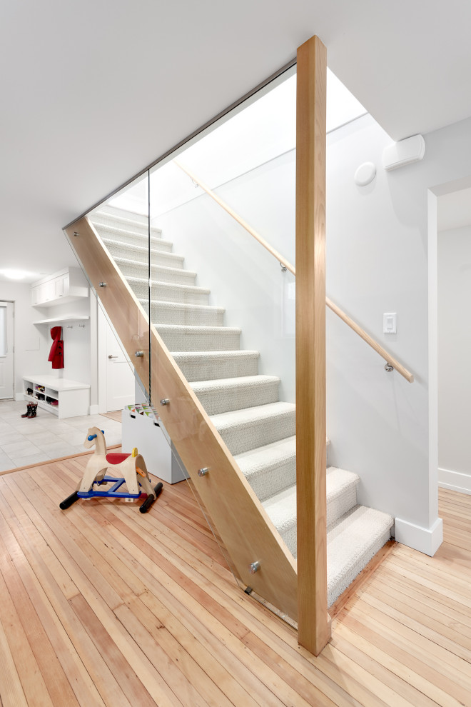 Design ideas for a mid-sized transitional carpeted straight staircase in Vancouver with glass risers and wood railing.
