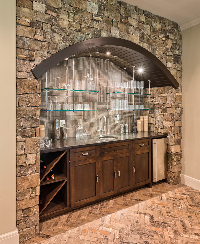 Design ideas for a mid-sized traditional single-wall wet bar in New York with an undermount sink, dark wood cabinets, granite benchtops, grey splashback, brick floors and recessed-panel cabinets.