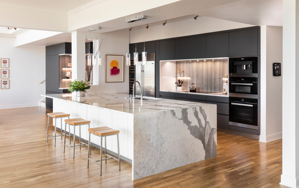 Design ideas for a contemporary galley open plan kitchen in Houston with an undermount sink, flat-panel cabinets, grey cabinets, grey splashback, black appliances, medium hardwood floors, with island, brown floor and grey benchtop.