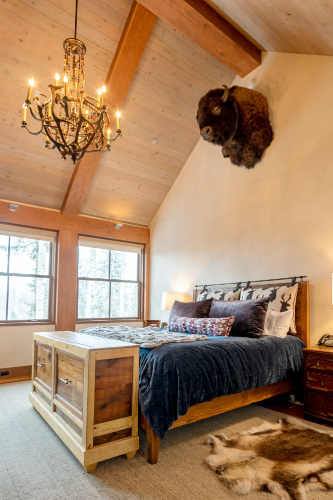 Cette photo montre une grande chambre parentale montagne avec un mur beige, un sol en bois brun et un plafond voûté.