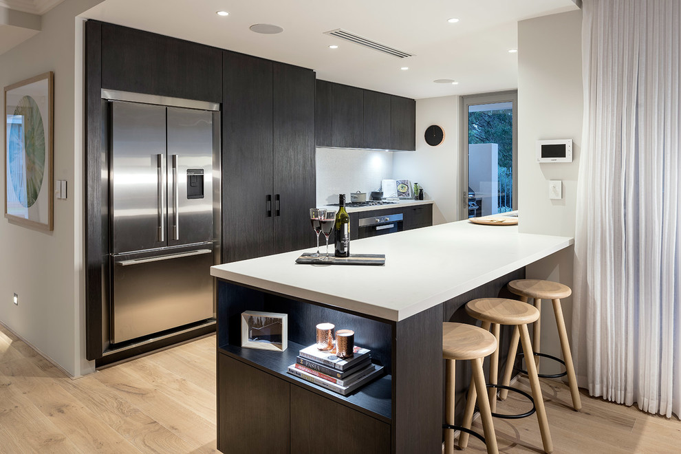 This is an example of a contemporary galley kitchen in Perth with flat-panel cabinets, dark wood cabinets, stainless steel appliances, light hardwood floors and a peninsula.
