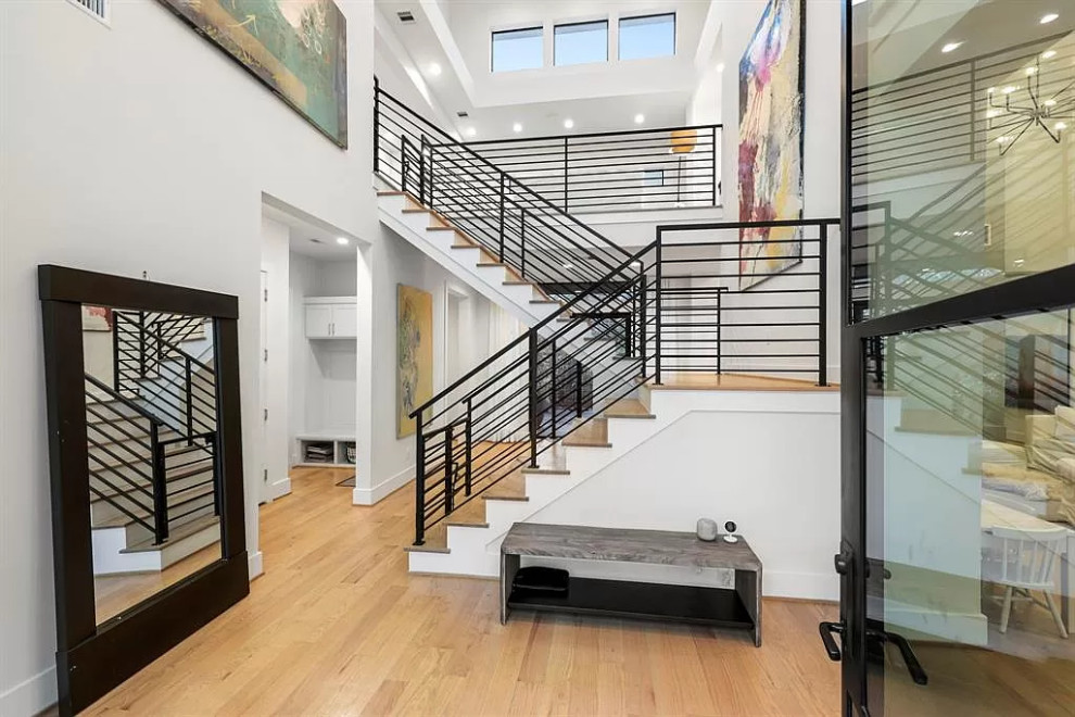 Cette image montre un grand escalier peint design en U avec des marches en bois et un garde-corps en métal.