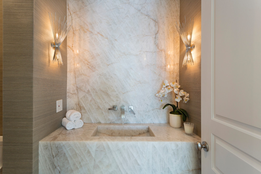 This is an example of a mid-sized beach style powder room in Other with brown walls, an integrated sink, marble benchtops, beige tile, stone slab and beige benchtops.