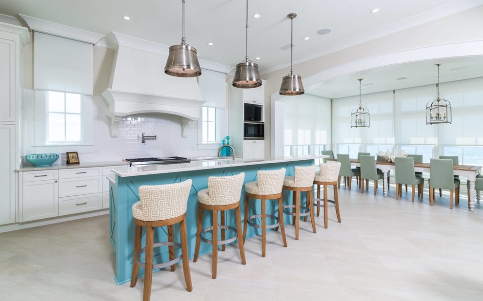 Beach style galley kitchen in Miami with shaker cabinets, white cabinets, white splashback, stainless steel appliances, with island and grey floor.