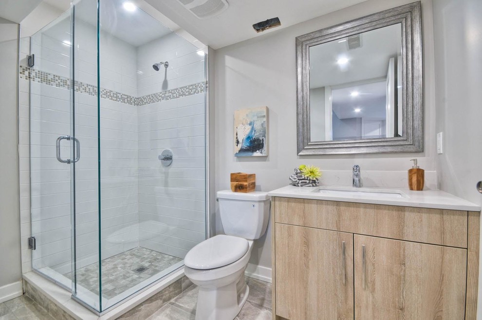 This is an example of a mid-sized transitional bathroom in Ottawa with flat-panel cabinets, light wood cabinets, a corner shower, a two-piece toilet, white tile, ceramic tile, grey walls, ceramic floors, an undermount sink, quartzite benchtops and a hinged shower door.