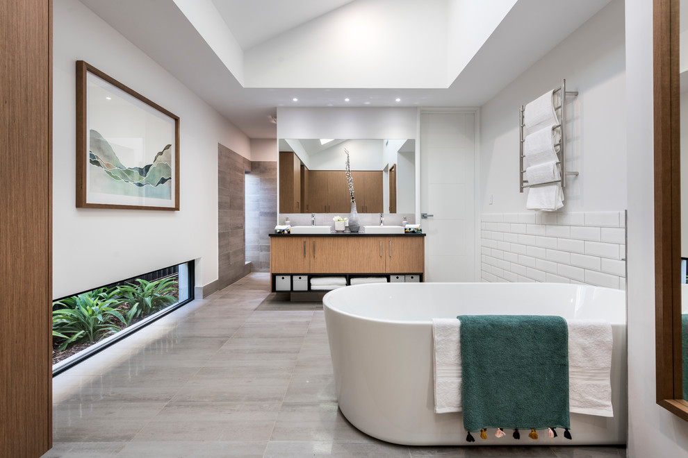 Inspiration for a contemporary kids bathroom in Perth with flat-panel cabinets, medium wood cabinets, a freestanding tub, an alcove shower, white tile, subway tile, white walls, a vessel sink, grey floor, an open shower and black benchtops.
