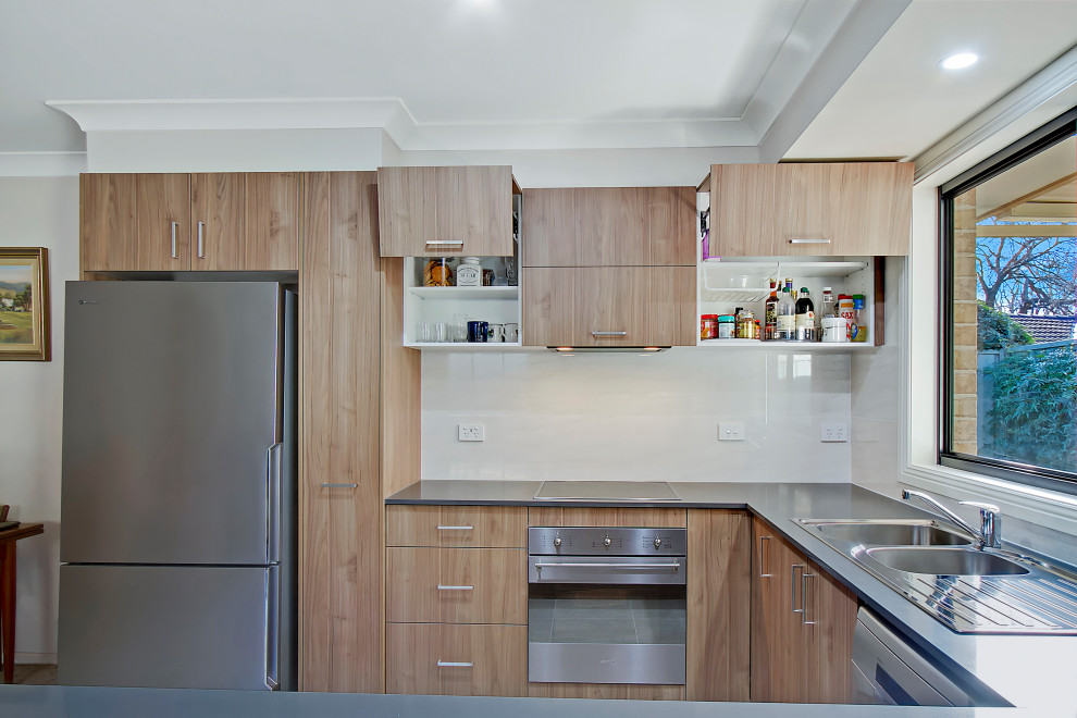 Inspiration for a mid-sized modern u-shaped eat-in kitchen in Sydney with a double-bowl sink, flat-panel cabinets, medium wood cabinets, quartz benchtops, white splashback, porcelain splashback, stainless steel appliances, beige floor and black benchtop.