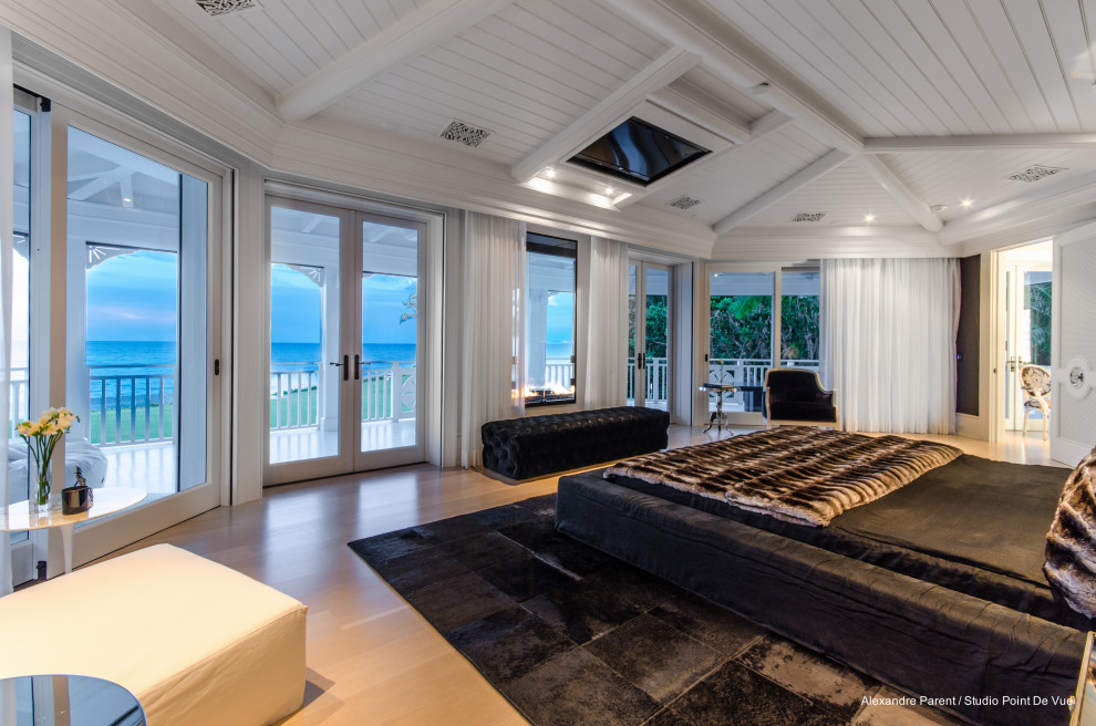 マイアミにある巨大なビーチスタイルのおしゃれな主寝室 (白い壁、淡色無垢フローリング、両方向型暖炉、ベージュの床、塗装板張りの天井) のインテリア