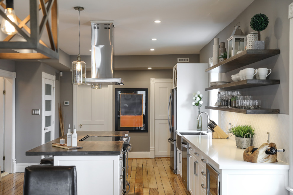 Eat-in kitchen - mid-sized transitional single-wall medium tone wood floor and brown floor eat-in kitchen idea with a farmhouse sink, shaker cabinets, white cabinets, white backsplash, stainless steel appliances, an island and white countertops